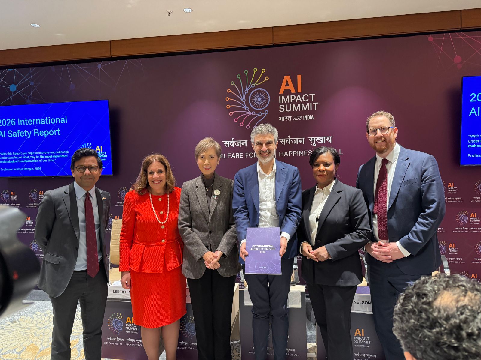 Lee Tiedrich with Yoshua Bengio and fellow contributors at the AI Impact Summit, holding the 2026 International AI Safety Report
